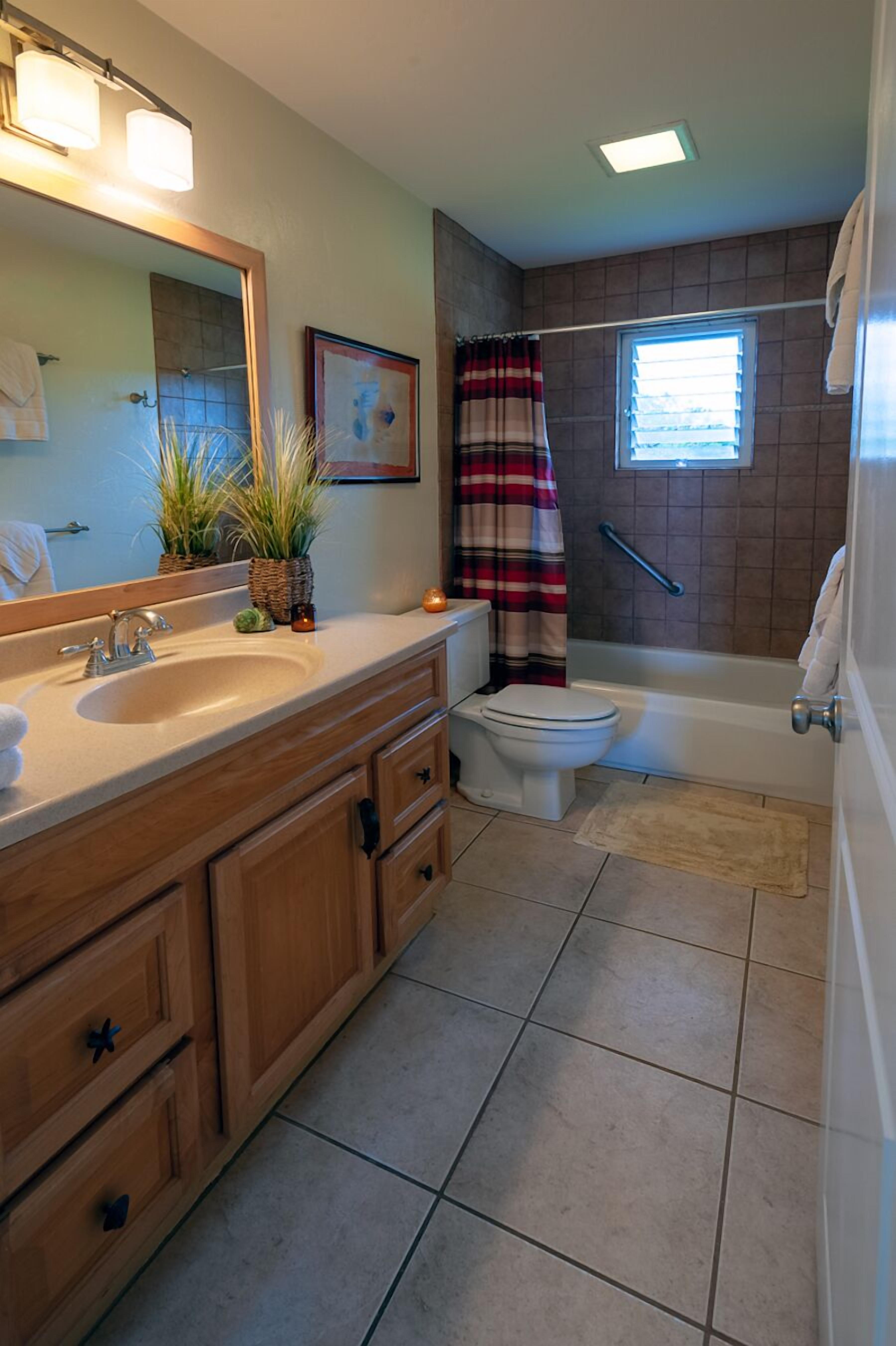 A bathroom with a sink, mirror, toilet, and shower area.