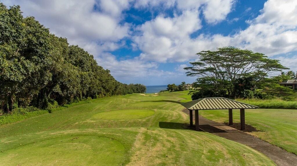 Un campo de golf con un pabellón, exuberante vegetación y cielo despejado.