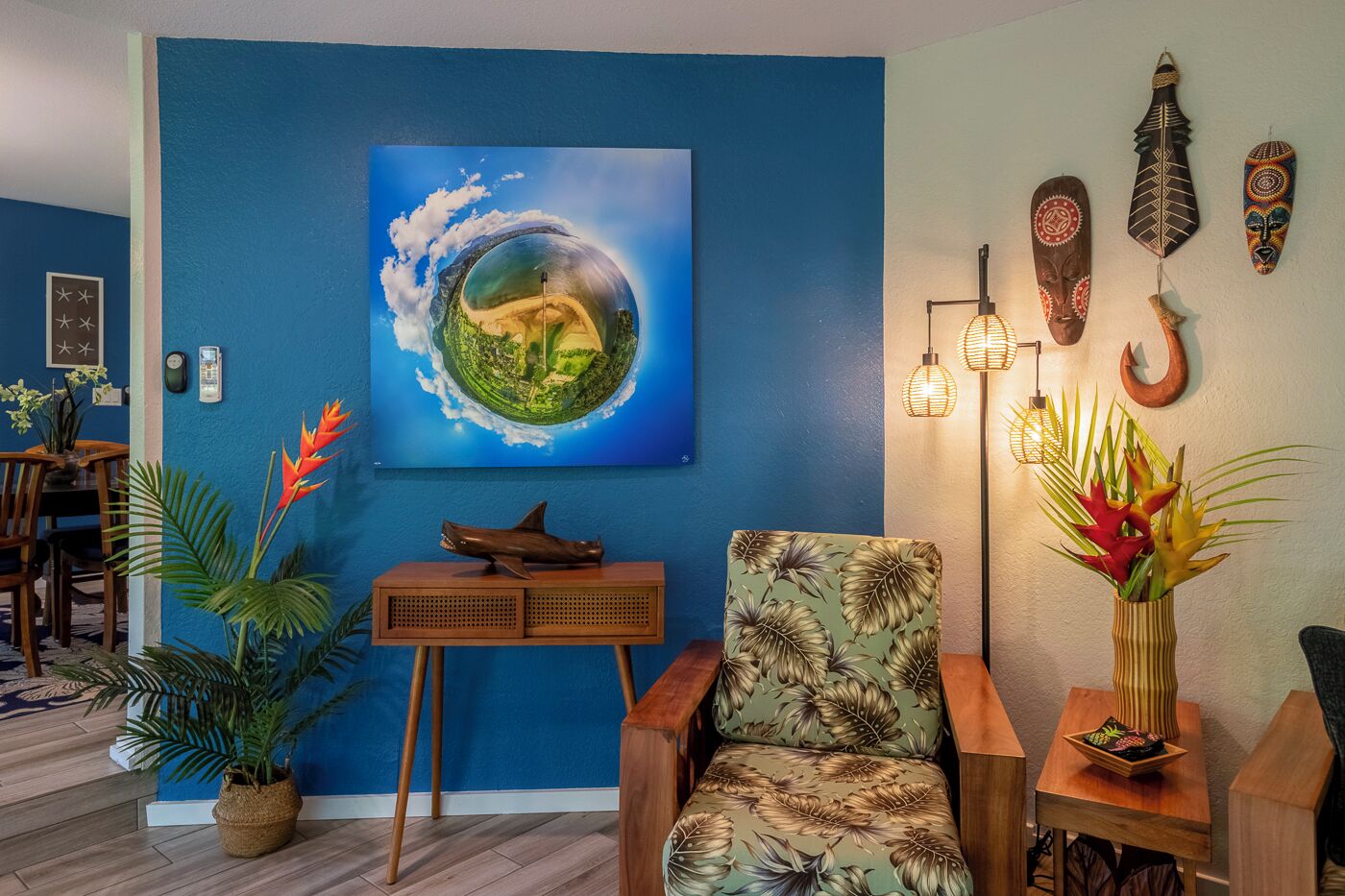 Una habitación con pared azul, un cuadro de un globo terráqueo, una mesa de madera, una silla con estampado de hojas y una lámpara de pie.