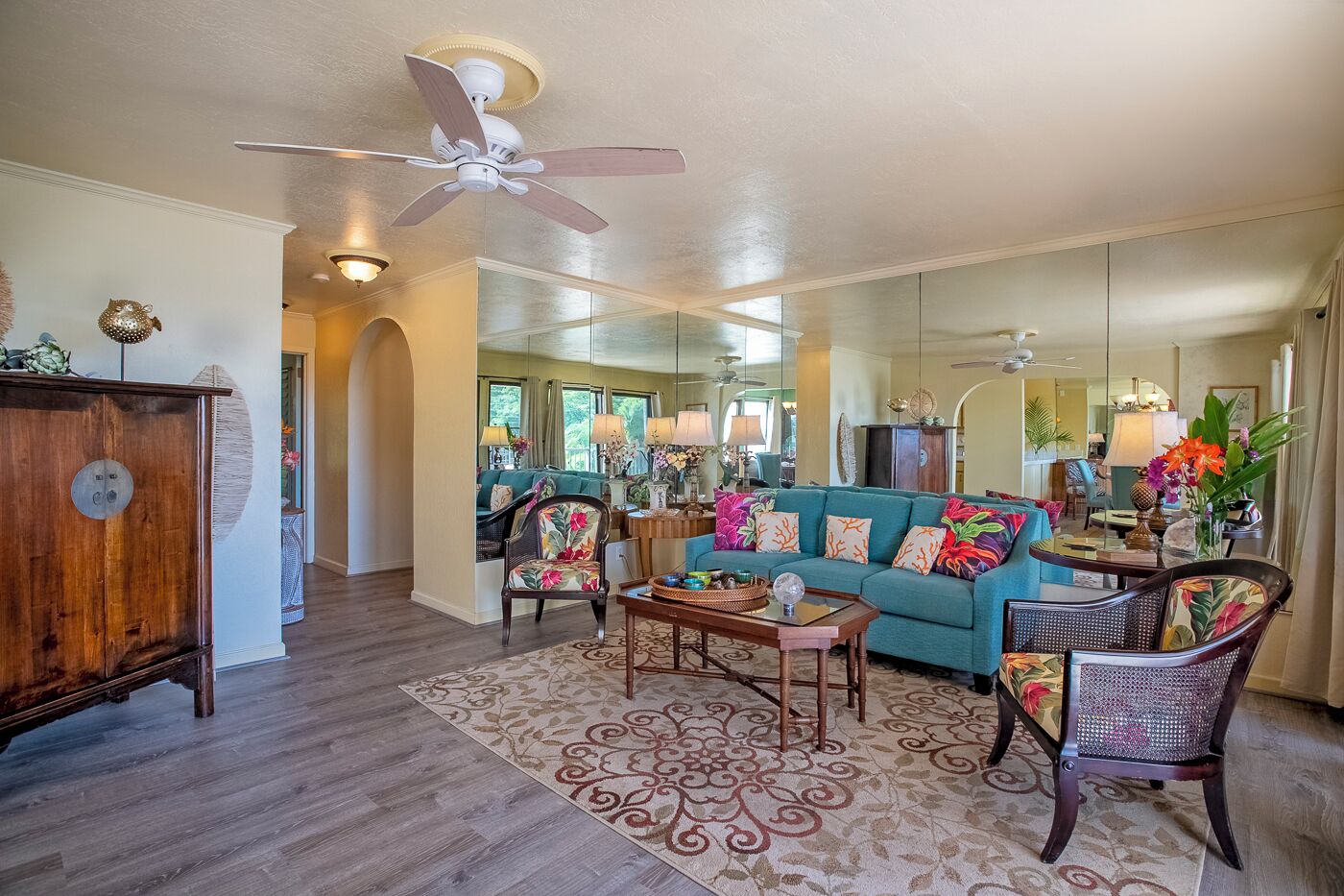 A spacious living room with a teal sofa, wooden coffee table, and a ceiling fan.