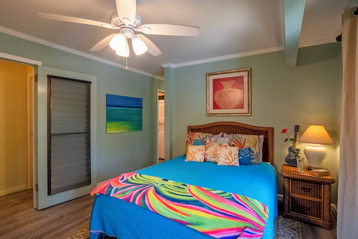 A bedroom with a bed, a ceiling fan, a nightstand with a lamp, and a framed picture on the wall.