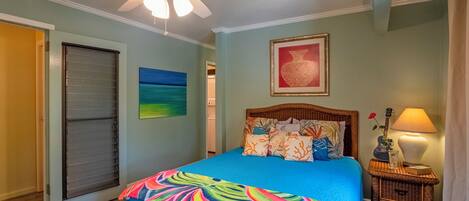 A bedroom with a bed, a ceiling fan, a nightstand with a lamp, and a framed picture on the wall.