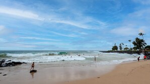 Una playa con olas, gente y palmeras.