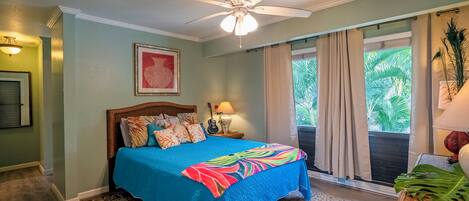 A bedroom with a bed, a ceiling fan, a window with curtains, and a view of greenery outside.