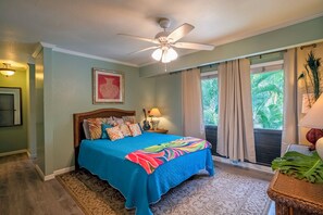 A bedroom with a bed, a ceiling fan, a window with curtains, and a view of greenery outside. - Kahala at Poipu Kai 123 (Koloa)