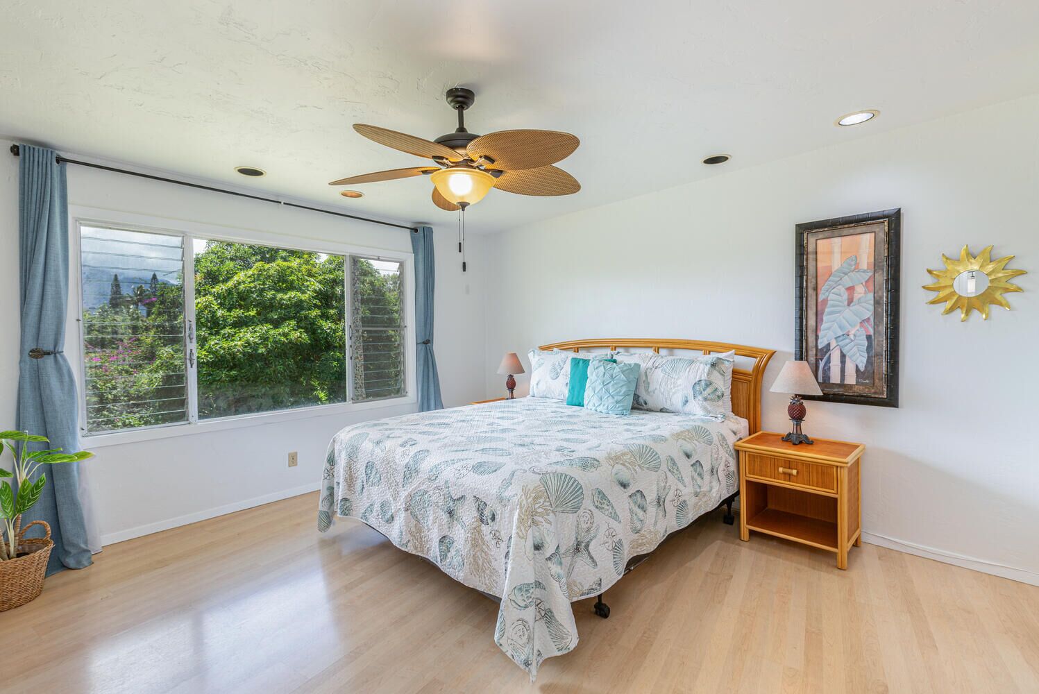 A bedroom with a bed, a ceiling fan, a nightstand, a lamp, a window with curtains, and a framed picture on the wall.