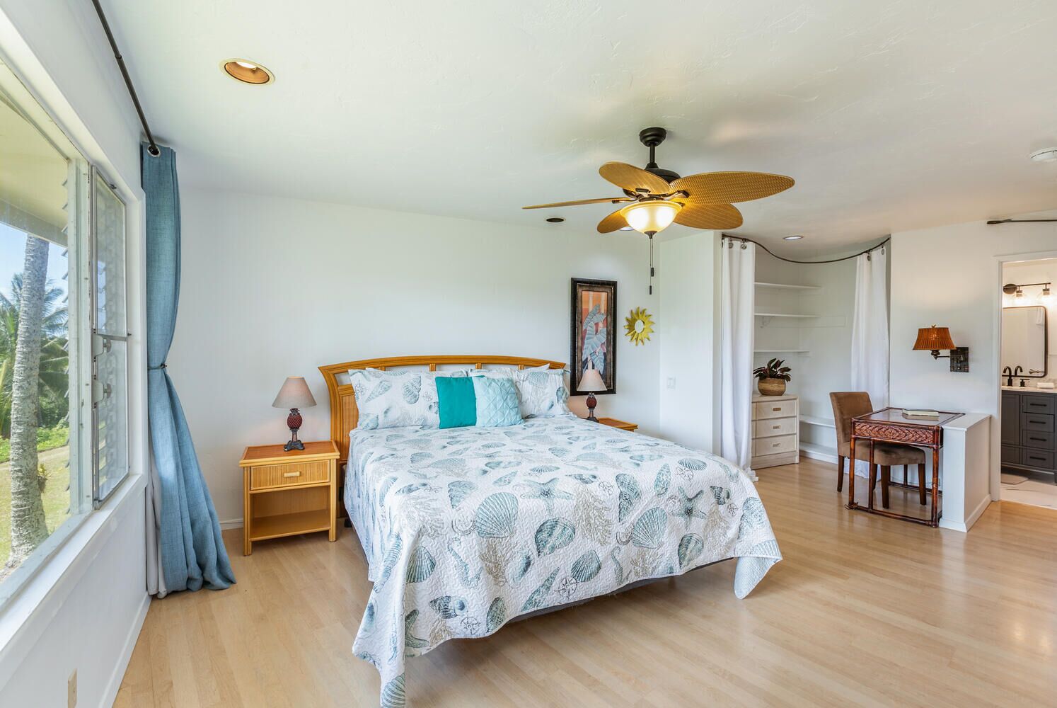 A bedroom with a bed, a desk, a chair, a ceiling fan, and a window with curtains.