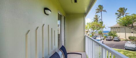 A balcony with two chairs, a railing, and a view of parked cars and palm trees.