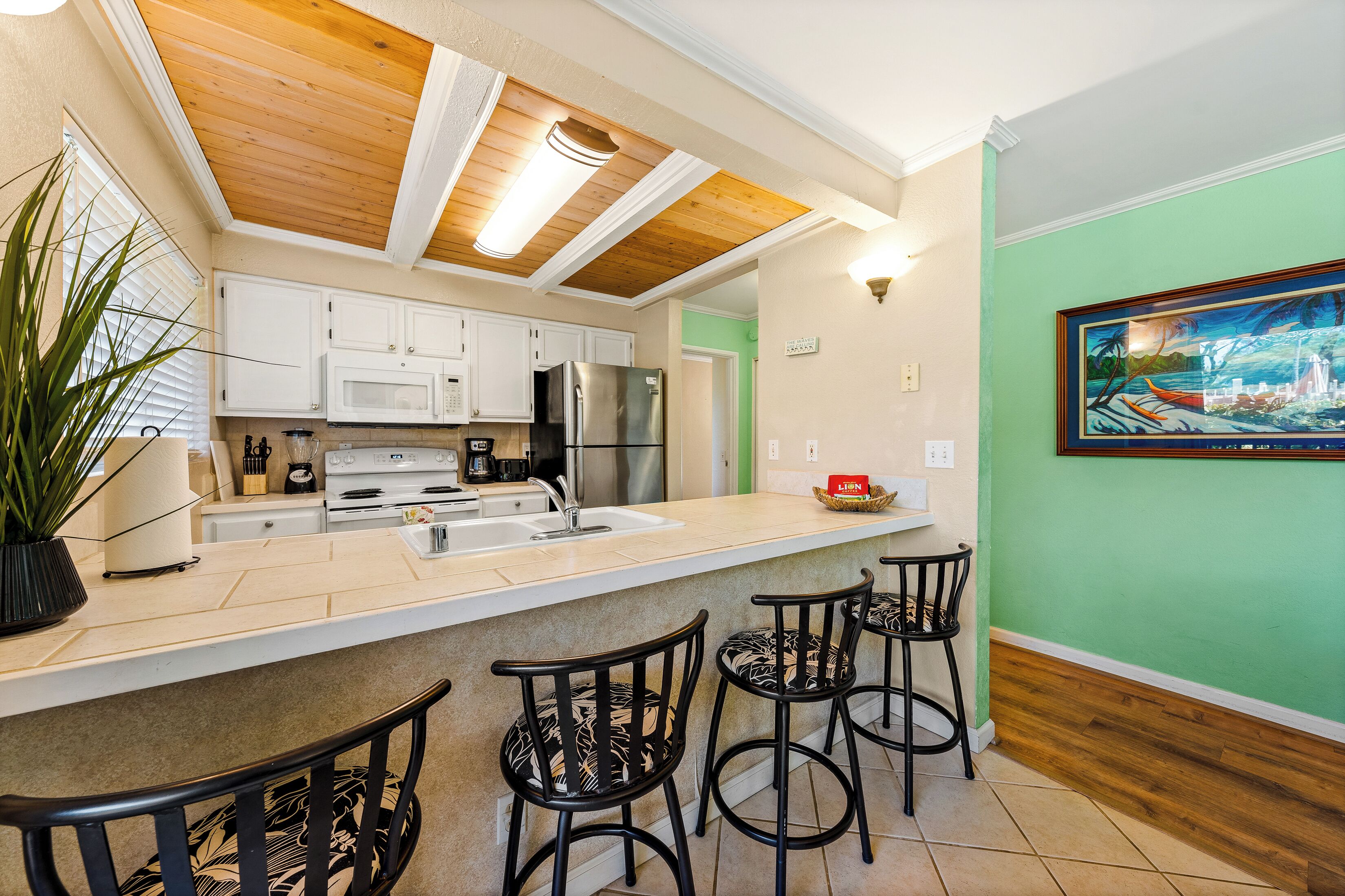 A kitchen with white cabinets, stainless steel appliances, a wooden ceiling, and a green wall with a framed picture.