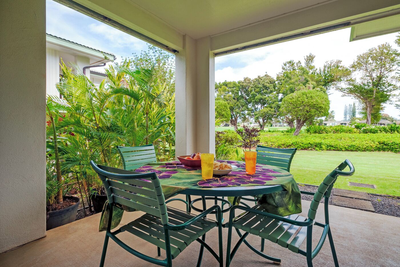 A covered patio with a table set for two, surrounded by lush greenery and a view of a well-maintained lawn and trees.