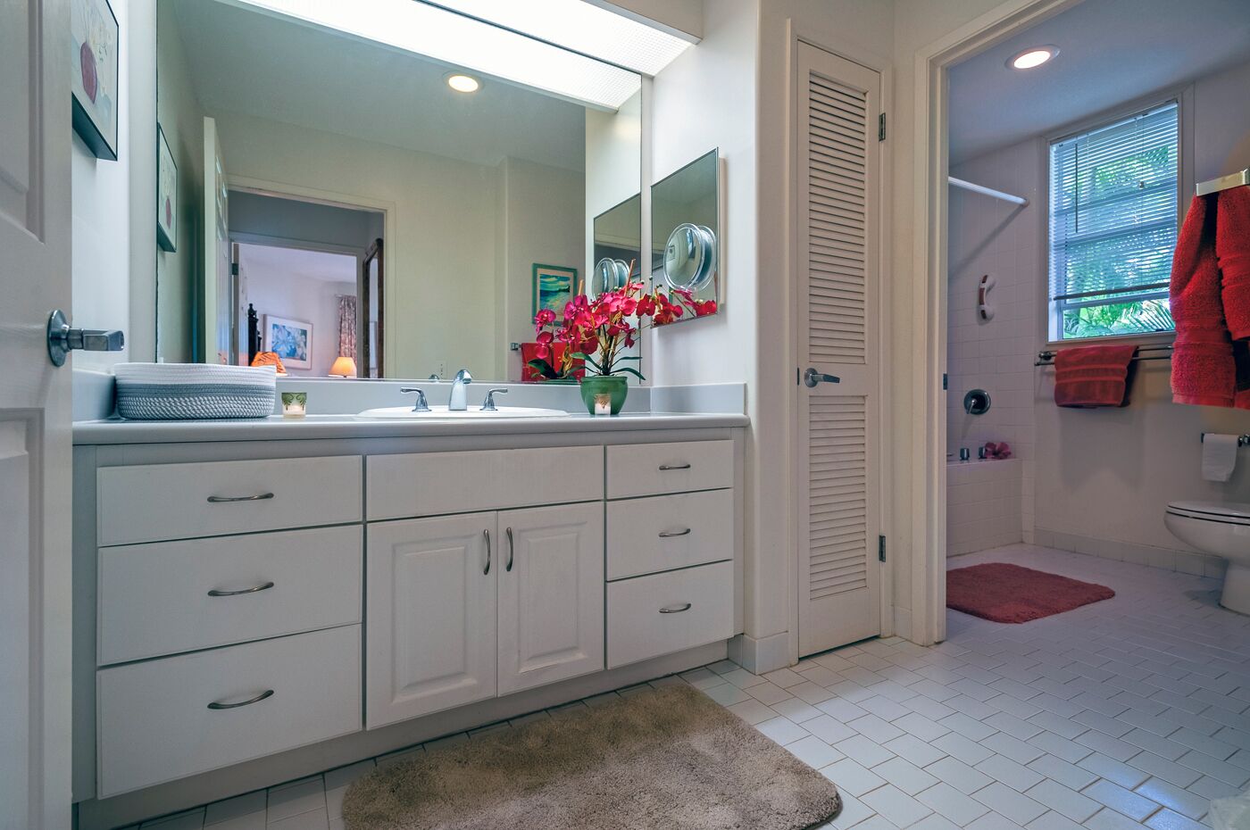 A modern bathroom with a large mirror, white cabinetry, a sink, and a shower area.