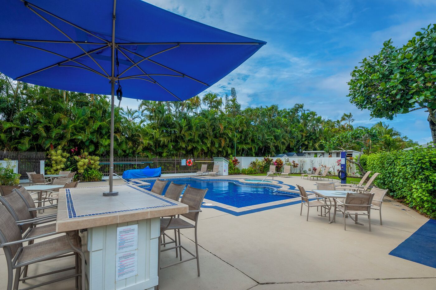 An outdoor pool area with lounge chairs and a table, surrounded by lush greenery.