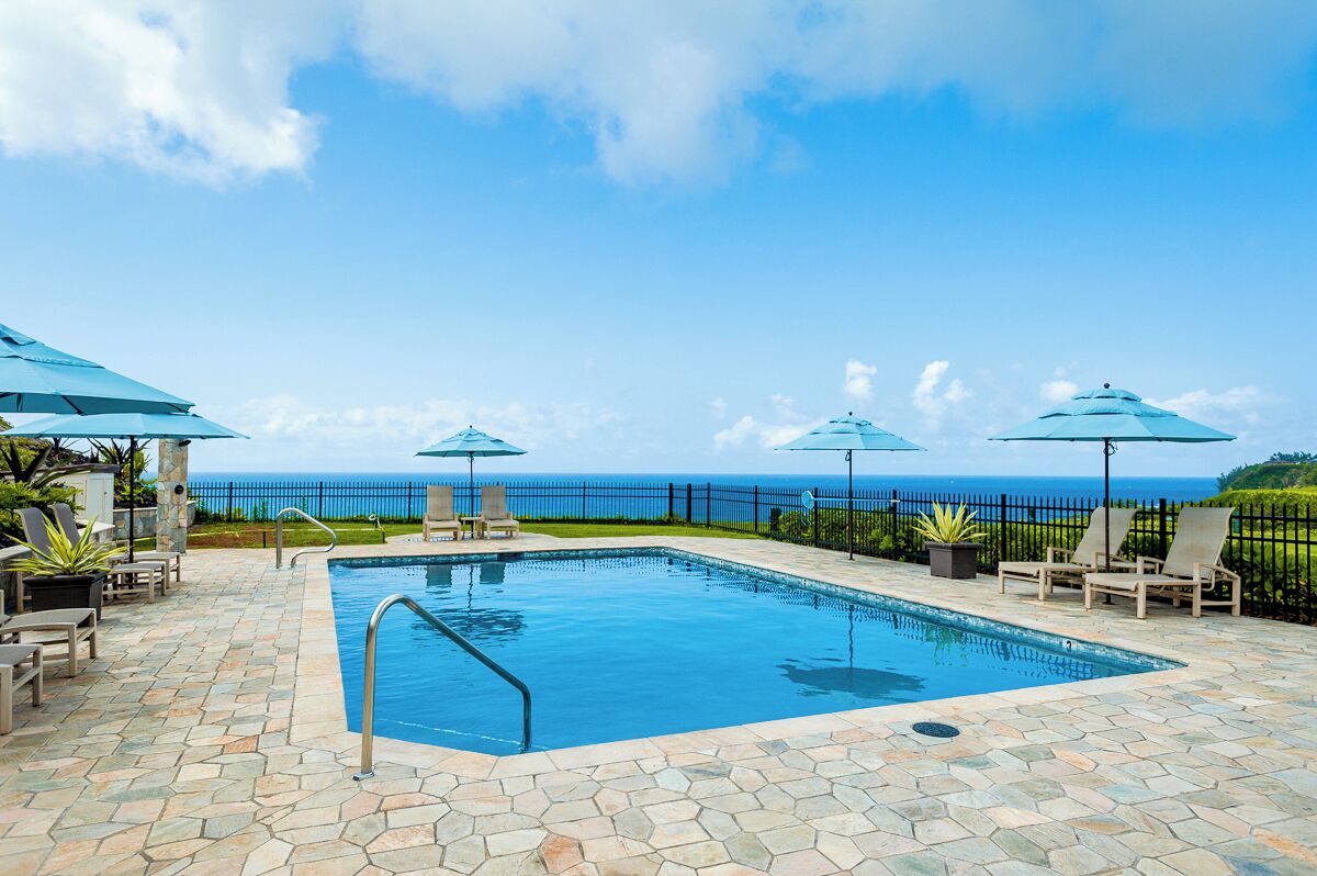 A swimming pool with a view of the ocean, surrounded by lounge chairs and umbrellas.