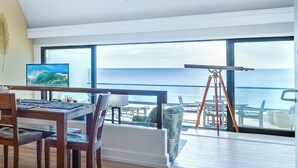 A modern room with a large window overlooking the sea, a dining area with wooden furniture, and a telescope on the windowsill. - Puu Poa 405 (Princeville)