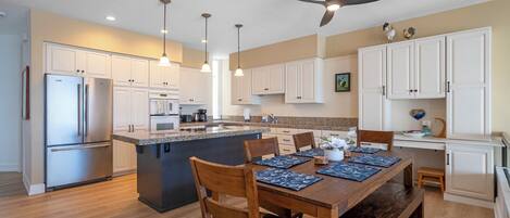 A modern kitchen with white cabinets, a stainless steel refrigerator, a central island with seating, pendant lights, and a ceiling fan.