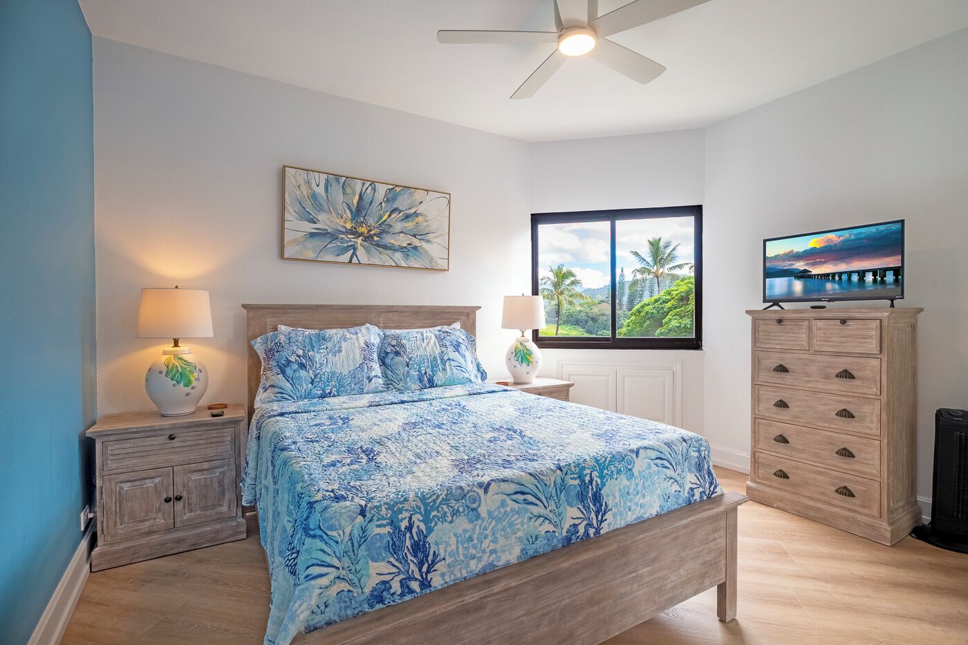 A bedroom with a bed, nightstands, a dresser, a ceiling fan, a window with a view, and a TV.