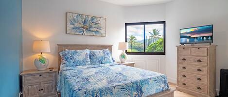 A bedroom with a bed, nightstands, a dresser, a ceiling fan, a window with a view, and a TV.