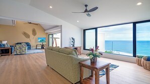A spacious living room with a large window offering a view of the ocean, a ceiling fan, and a modern interior design. - Puu Poa 405 (Princeville)