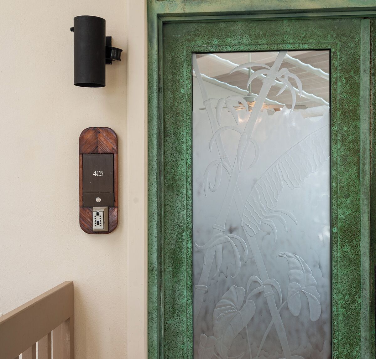 A door with frosted glass and a green frame, a wall-mounted intercom, and a doorbell with a wooden design.