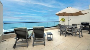 A balcony with a view of the ocean, a table with chairs, a grill, and a potted plant. - Puu Poa 405 (Princeville)
