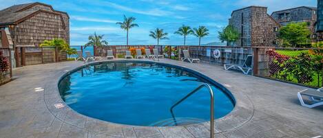 A swimming pool with lounge chairs and a view of the ocean.