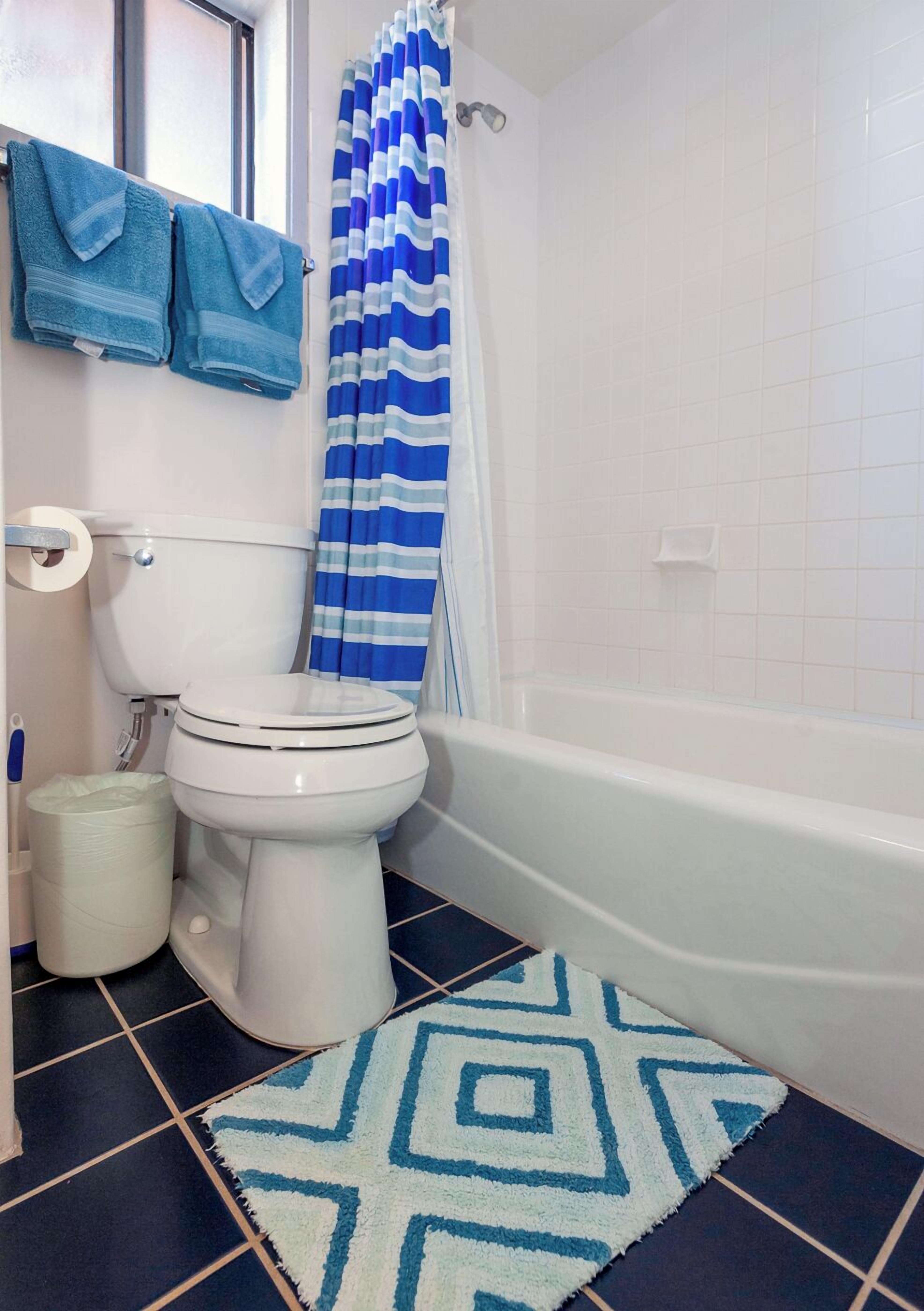 A bathroom with a toilet, a bathtub, a shower curtain, and a patterned rug.
