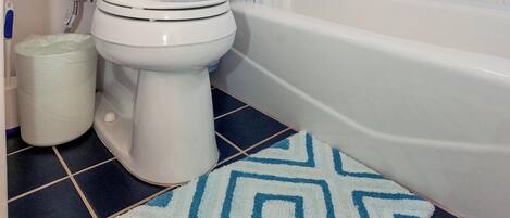A bathroom with a toilet, a bathtub, a shower curtain, and a patterned rug.