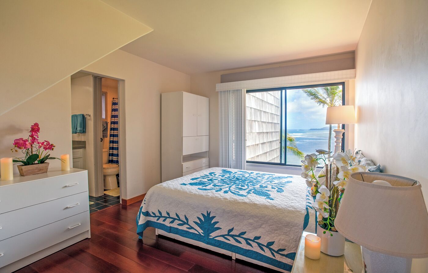 Un dormitorio con una cama grande, una ventana con vistas, un aparador blanco y una mesita de noche con lámpara.