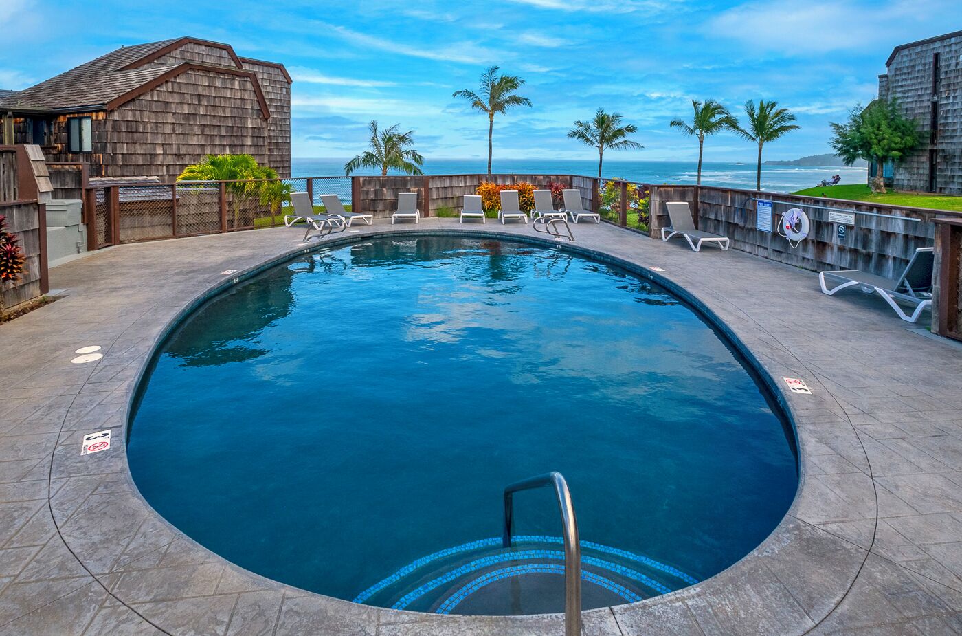 Piscina com vista clara do oceano, rodeada por espreguiçadeiras e palmeiras.