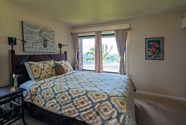 A hotel room with a large bed, a view of the beach, a painting on the wall, and a small table with a vase. - Sealodge G8 (Princeville)