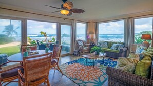 A spacious room with a large window overlooking the ocean, a ceiling fan, and a dining area with wicker furniture. - Hanalei Colony Resort I-1 (Hanalei)
