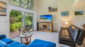 A spacious living room with a large TV, comfortable seating, and a view of the outdoors through a sliding glass door.