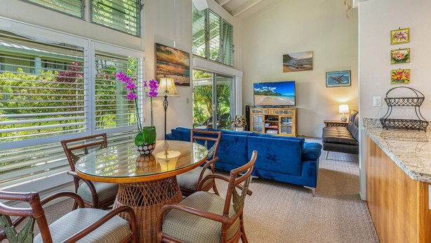 A spacious living area with a glass dining table, blue sofa, and a television.