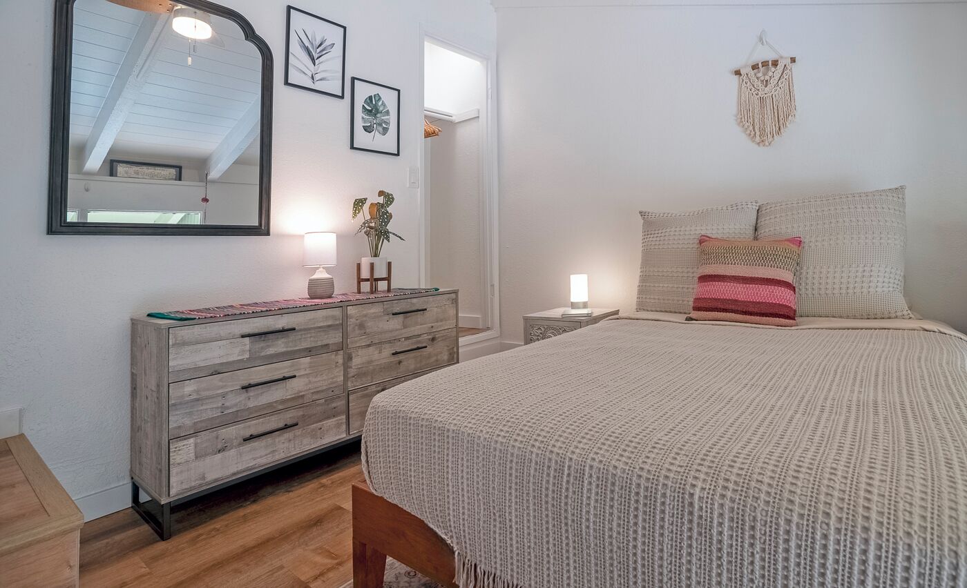 A bedroom with a bed, a dresser, a mirror, and wall decor.
