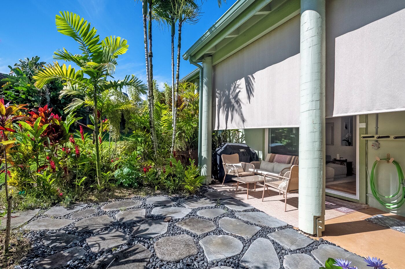 Une terrasse dotée d’un sol en pierre, de mobilier d’extérieur et d’une végétation tropicale luxuriante.