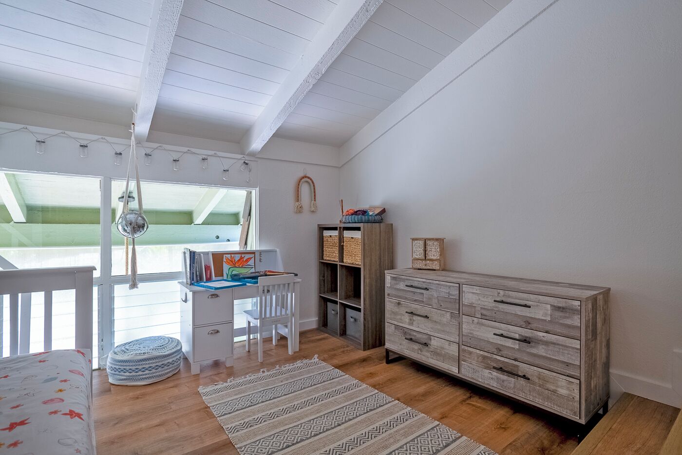 A room with a wooden desk, a white chair, a bookshelf, and a dresser.