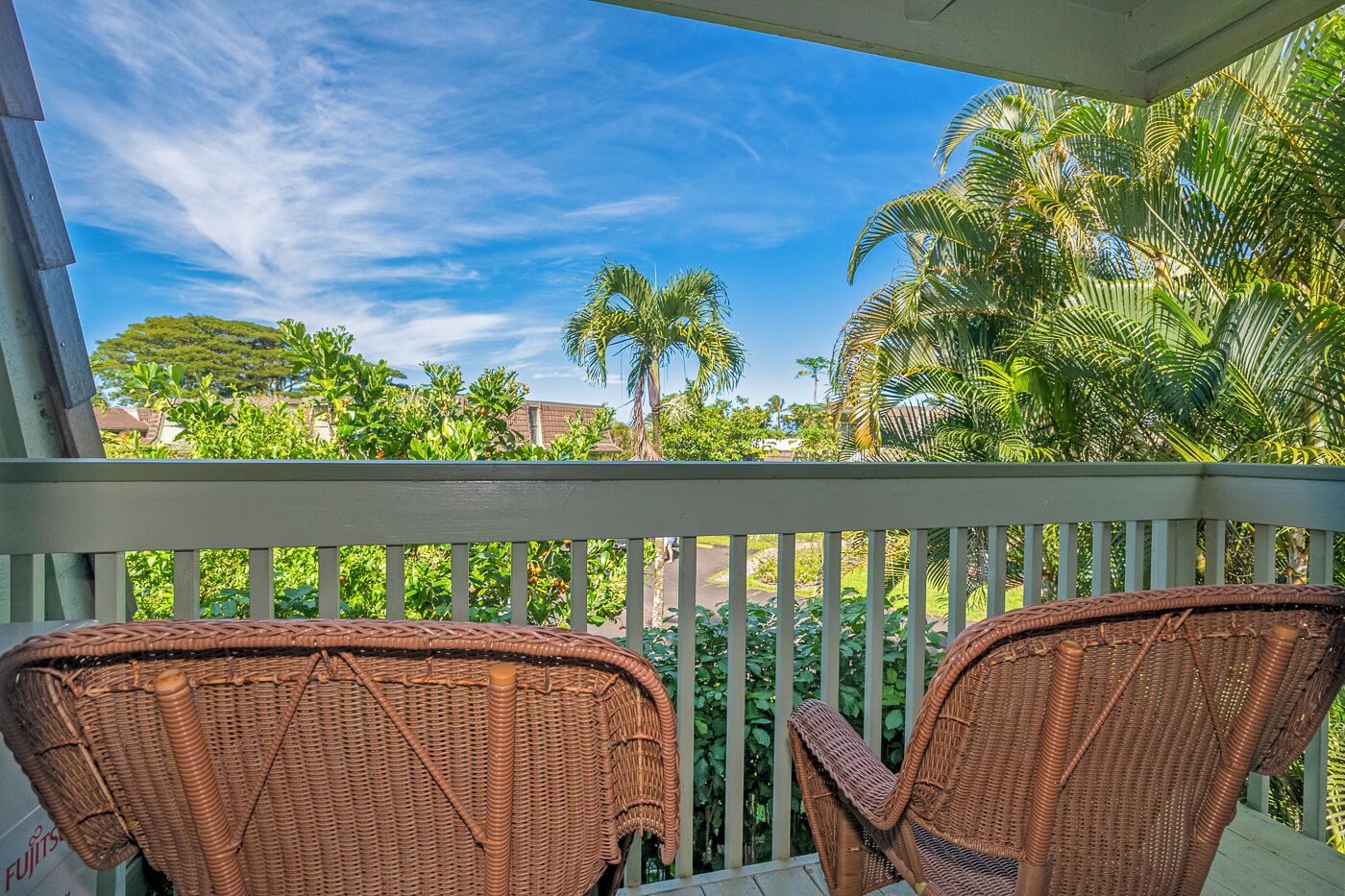 A balcony with wicker chairs and a view of palm trees and greenery.