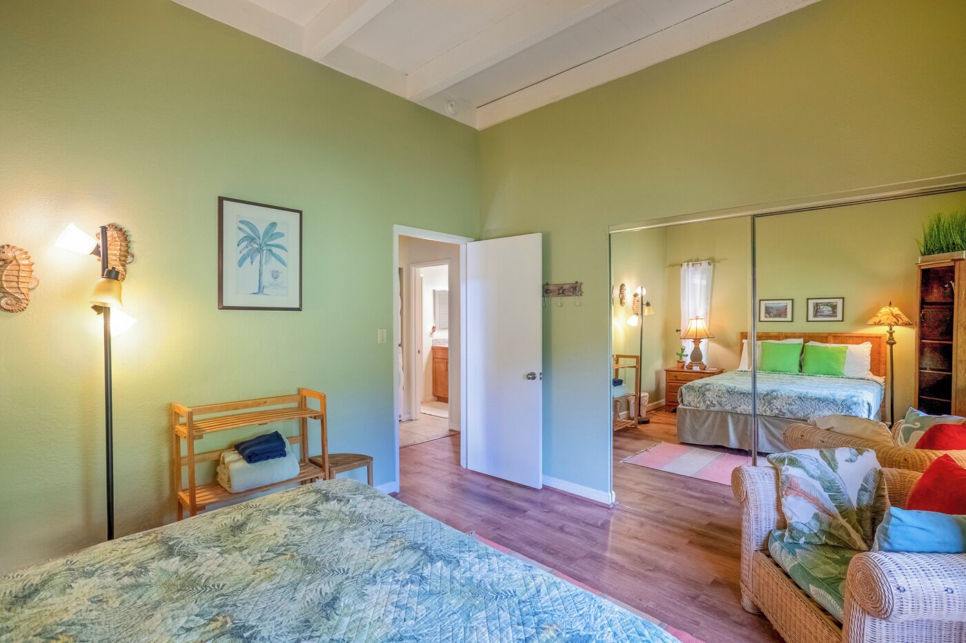 A bedroom with a bed, a chair, a bedside table, and a mirror. There is a door leading to another room.