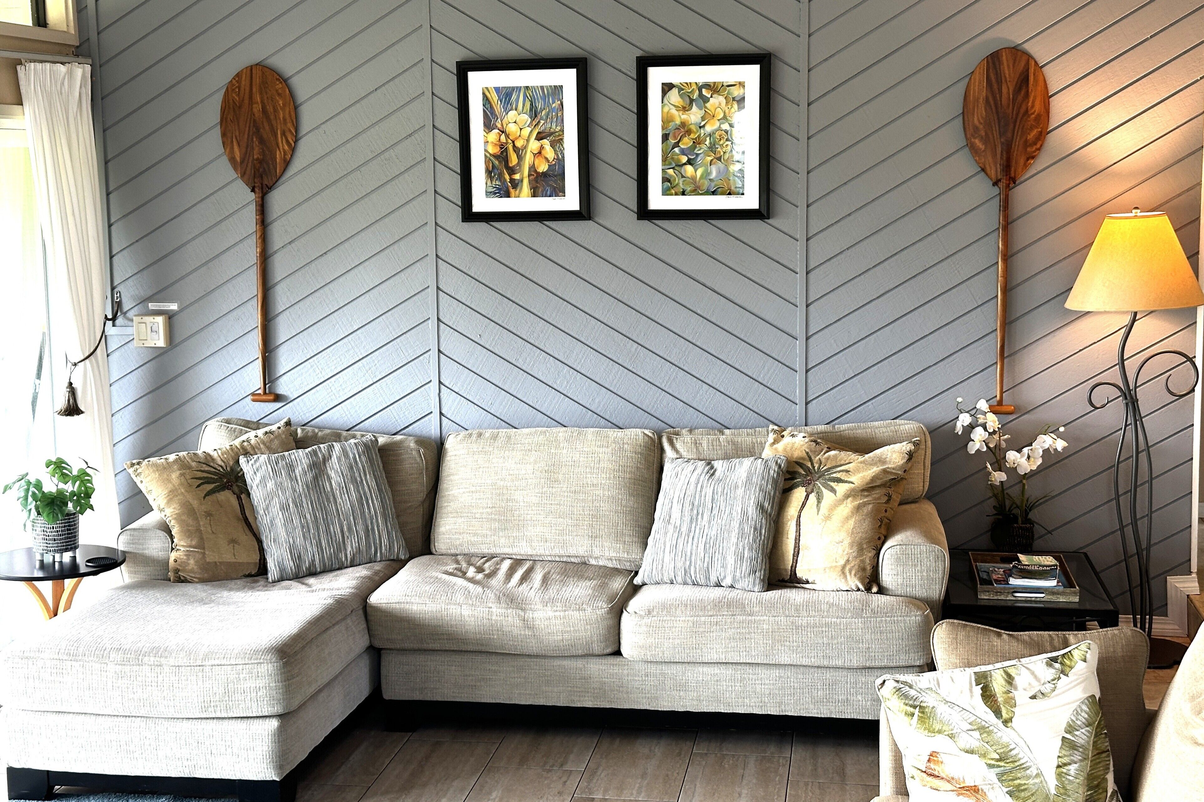 A modern living room with a sectional sofa, two framed artworks, a floor lamp, and a small side table with a plant.