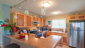 A modern kitchen with wooden cabinets, a central island, stainless steel appliances, and pendant lighting. - Kamahana 23 (Princeville)