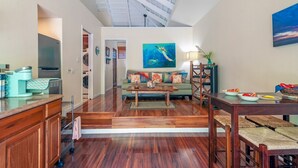 A spacious living area with a high ceiling, a dining table with chairs, a sofa with colorful cushions, and a painting of a sea creature. - Paniolo 210b (Princeville)