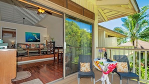 A modern living room with a glass wall, wooden flooring, and a dining area with a table and chairs. - Paniolo 210b (Princeville)