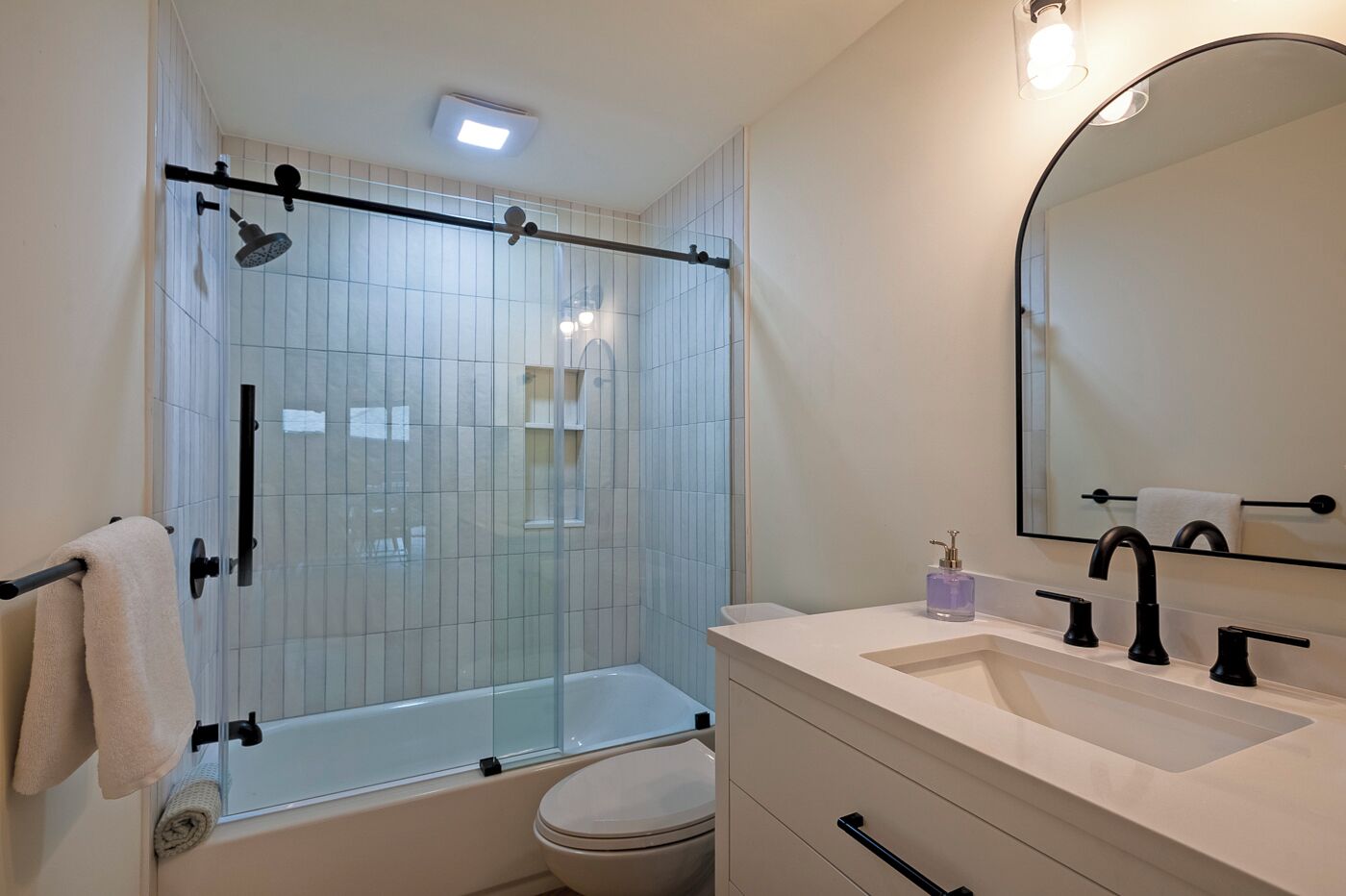 A modern bathroom with a glass shower enclosure, a white sink with black faucets, and a large mirror.