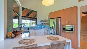 Une cuisine moderne dotée d’un grand îlot central, d’appareils électroménagers en acier inoxydable et de chaises en osier.