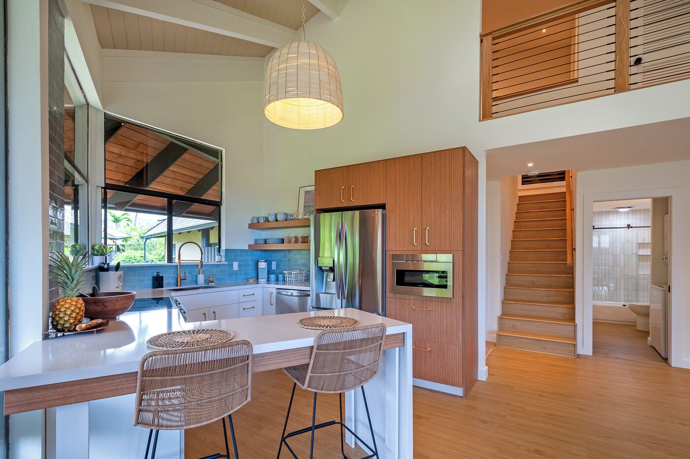 A modern kitchen with a central island, stainless steel appliances, and a wooden staircase leading to another level.