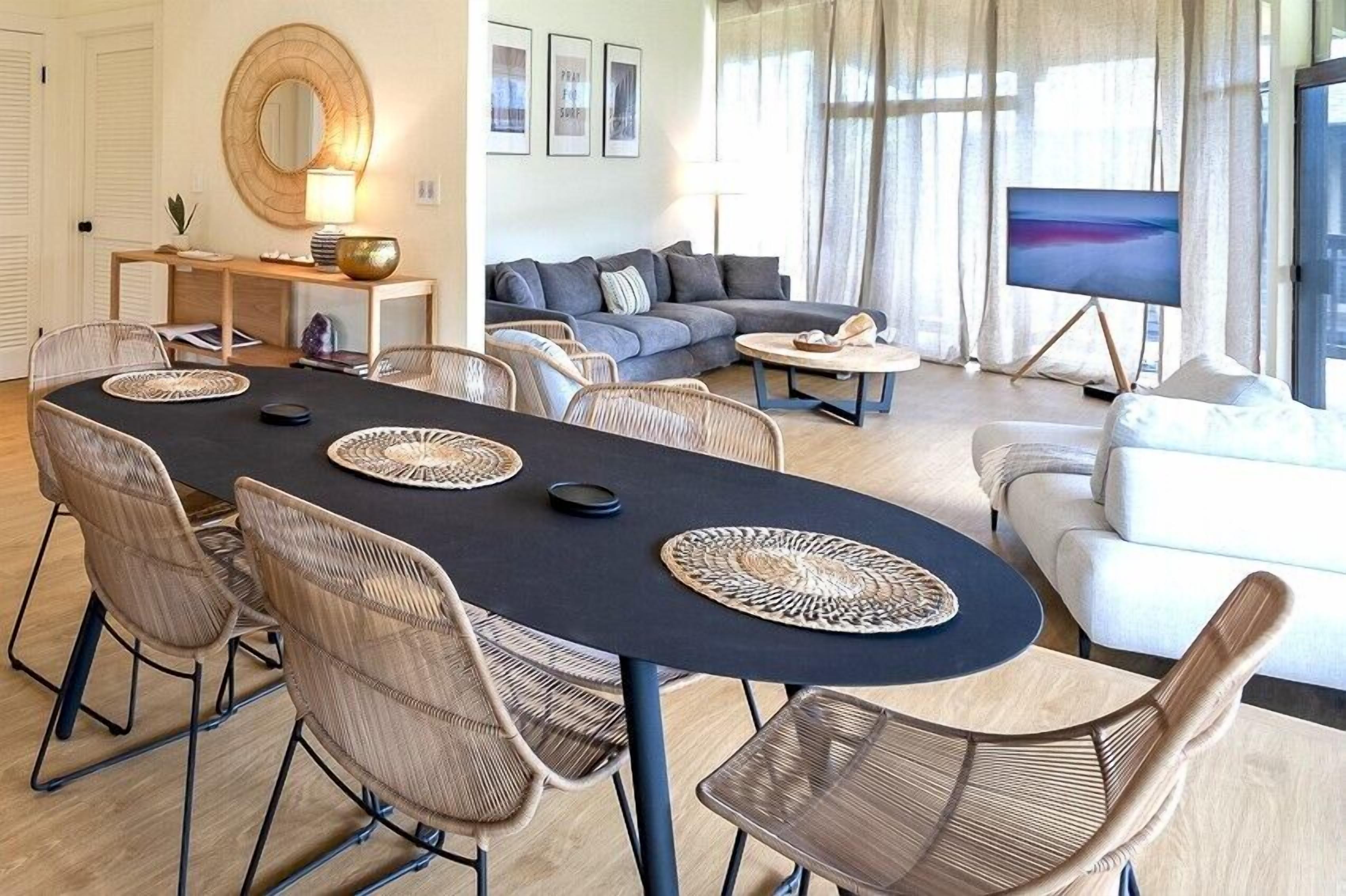 A modern living room with a dining area, a sofa, a TV, and a large window with curtains.