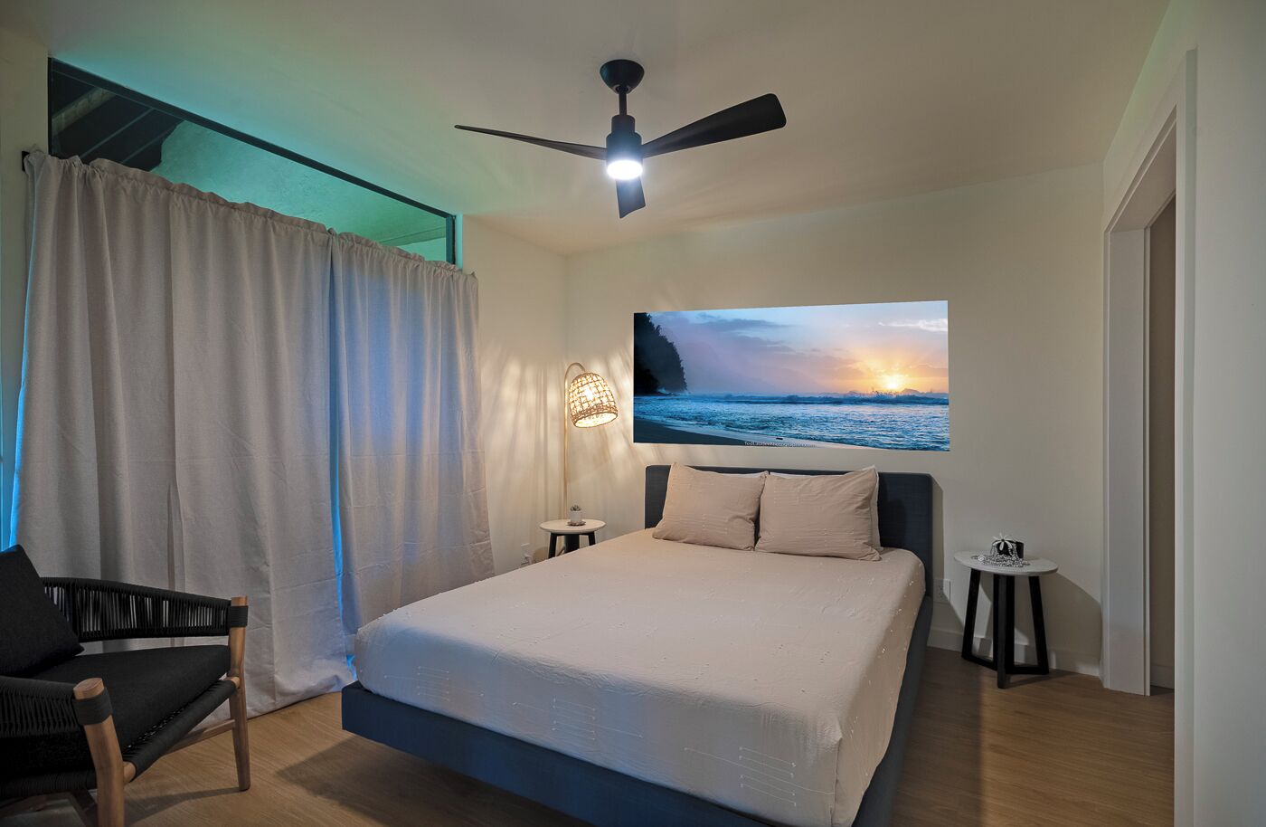 A modern bedroom with a bed, a ceiling fan, a nightstand, a chair, and a wall-mounted lamp.