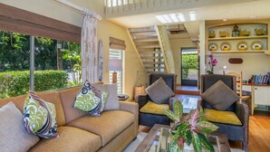 Un vaste espace de vie comprenant un canapé, des fauteuils, une table basse et un escalier menant à un niveau supérieur.
