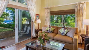Un salon spacieux, doté d’un canapé, d’une table basse et offrant une vue sur un jardin luxuriant et des palmiers.