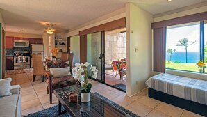 A modern living room with a sofa, coffee table, and a view of the ocean through large windows. - Sealodge F1 (Princeville)
